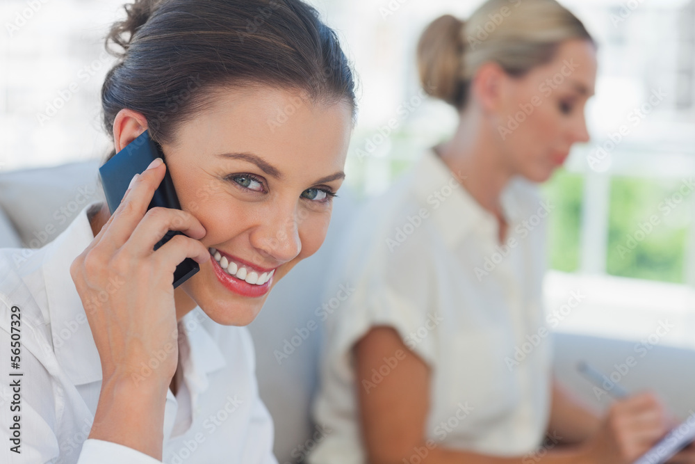 Businesswoman having a call while her colleague writing Businesswoman having a call while her colleague writing