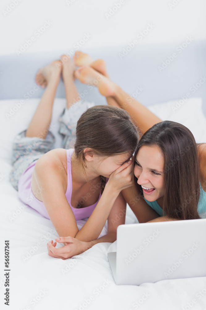 Friends lying in bed in pajamas with laptop Friends lying in bed in pajamas with laptop