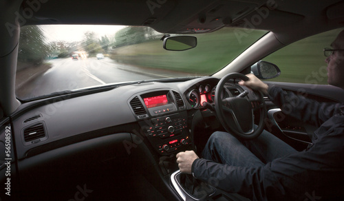 A man driving a car at speed in wet weather conditions.