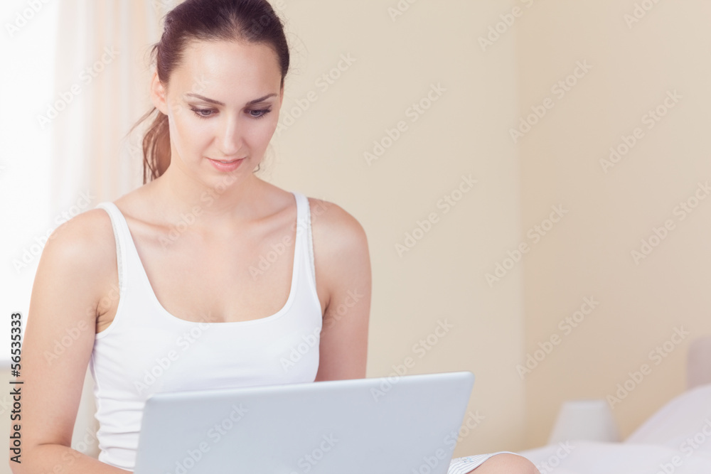 Smiling brunette sitting on bed using her laptop Smiling brunette sitting on bed using her laptop