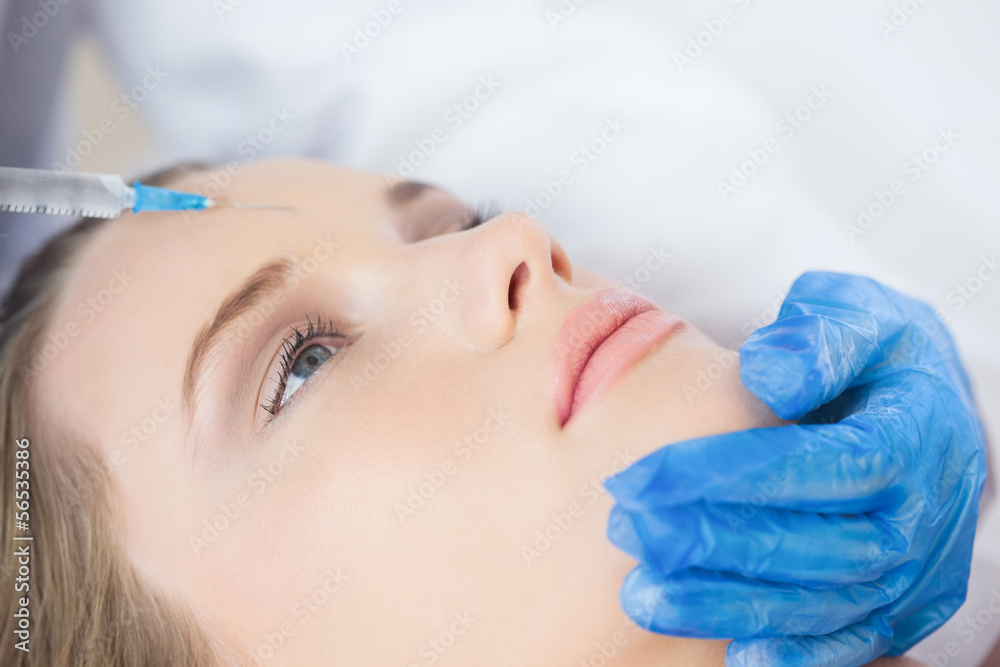 Surgeon making injection on forehead on calm woman lying Surgeon making injection on forehead on calm woman lying