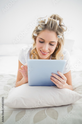 Cheerful pretty blonde wearing hair curlers scrolling on tablet