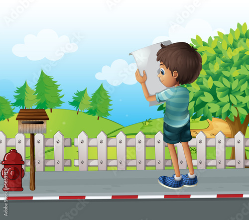 A boy with a paper standing near the fence at the street