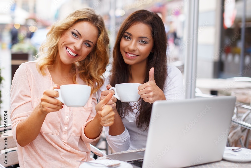 Two beautiful girls cups and laptop in summer cafe Two beautiful girls cups and laptop in summer cafe