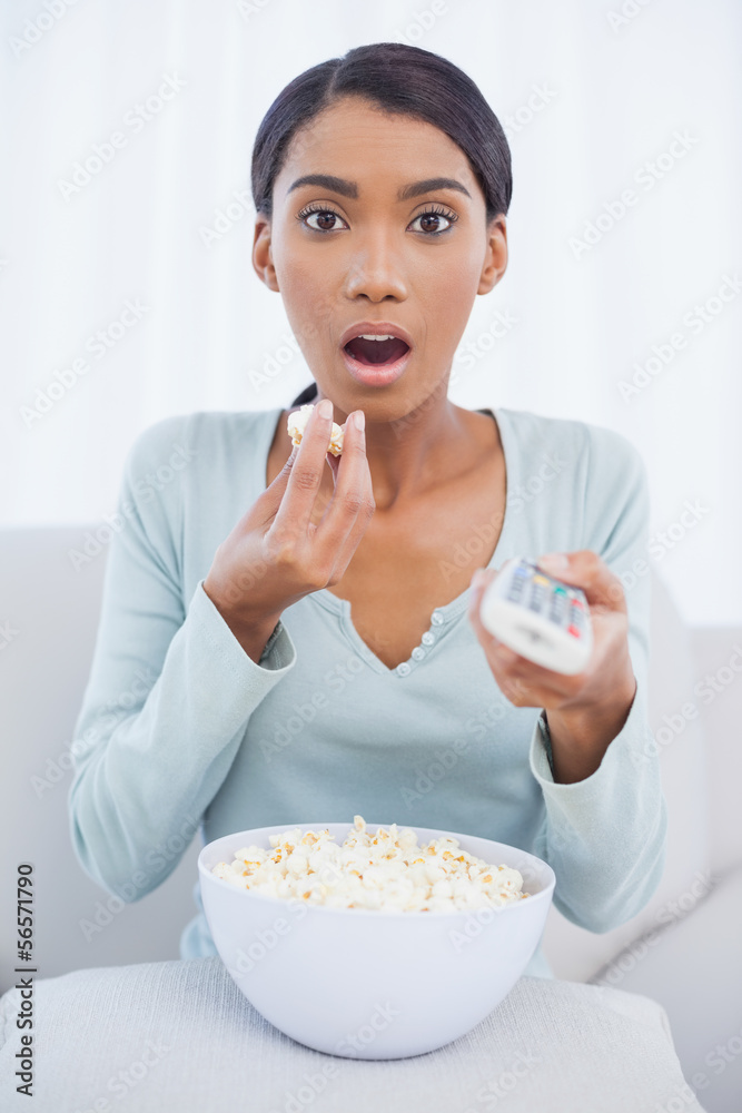 Astonished attractive woman eating popcorn while watching tv Astonished attractive woman eating popcorn while watching tv