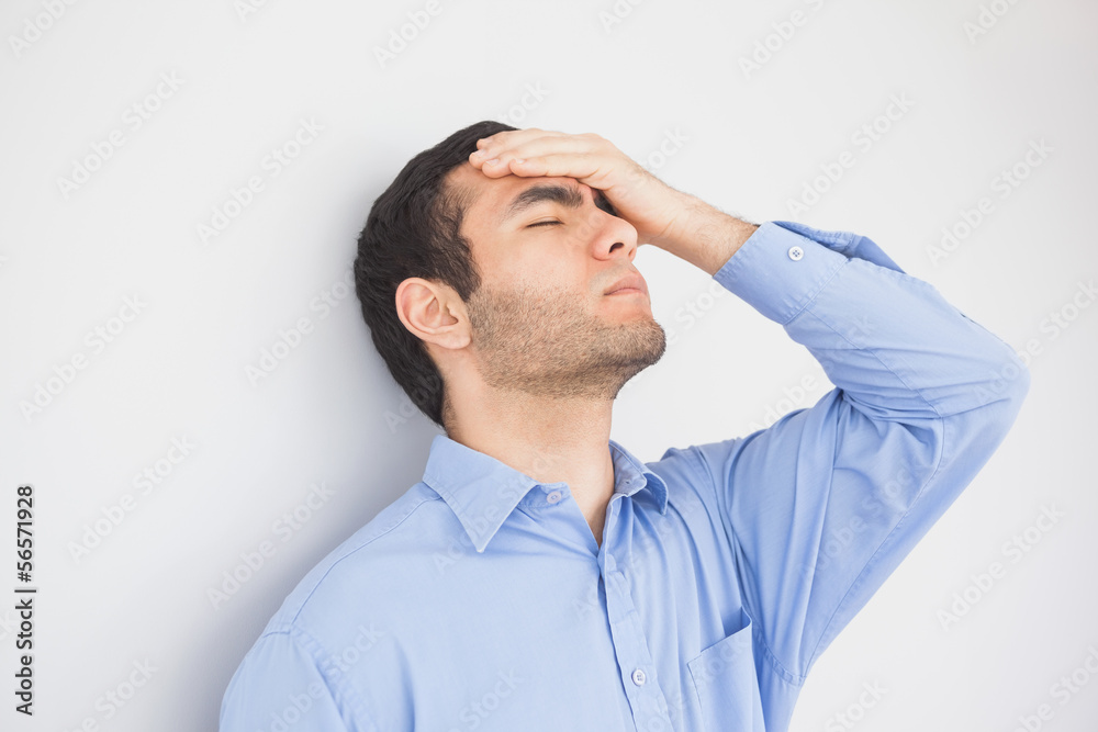 Irritated man with hand on forehead leaning against a wall Irritated man with hand on forehead leaning against a wall
