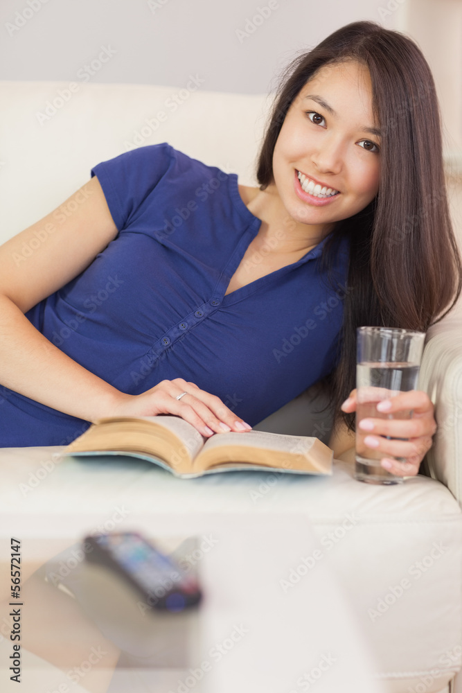 Pretty asian girl lying on the sofa reading a novel and drinking Pretty asian girl lying on the sofa reading a novel and drinking