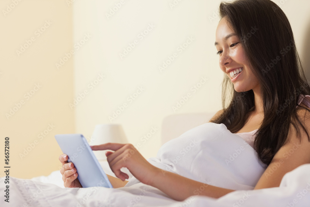 Smiling young asian woman sitting in bed using tablet pc Smiling young asian woman sitting in bed using tablet pc