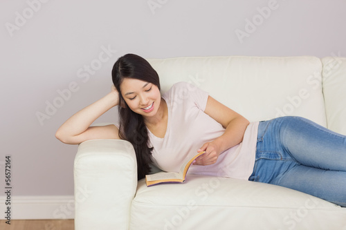 Pretty asian girl lying on the sofa reading book