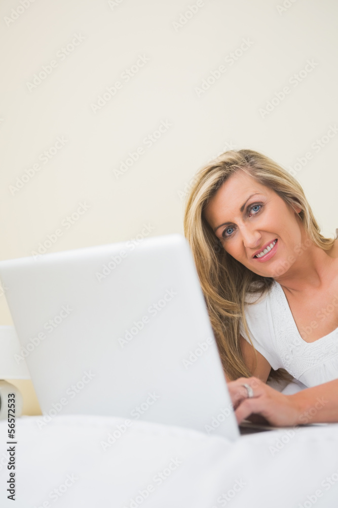 Amused woman typing on a laptop lying on her bed Amused woman typing on a laptop lying on her bed