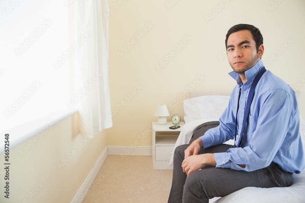 Stern man looking at camera and relaxing sitting on his bed