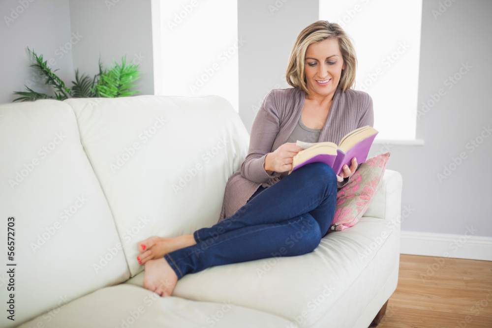 Smiling woman lying on a sofa reading a book Smiling woman lying on a sofa reading a book
