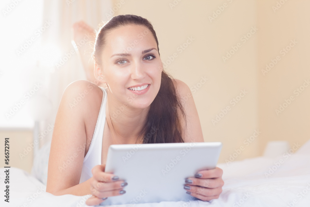 Happy brunette lying on bed with her tablet pc Happy brunette lying on bed with her tablet pc