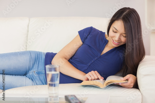 Happy asian girl lying on the sofa reading a novel © WavebreakmediaMicro