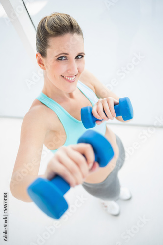 Fit smiling woman exercising with dumbbells