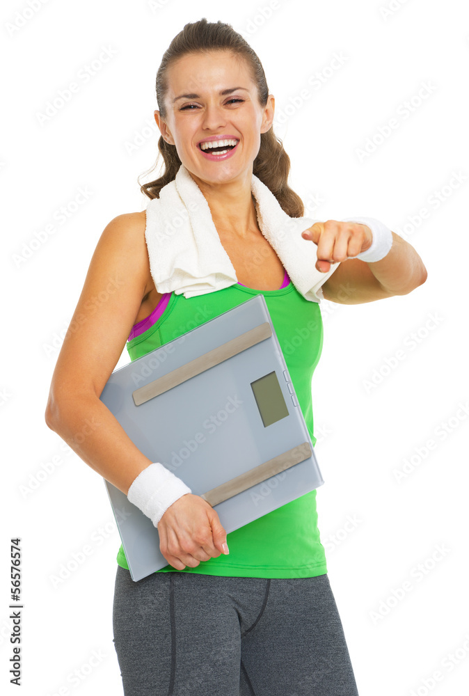 Smiling fitness young woman with scales pointing in camera Smiling fitness young woman with scales pointing in camera