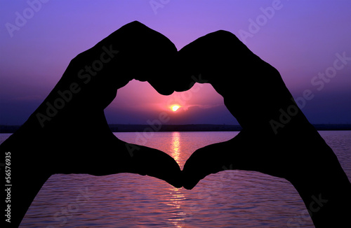 Woman's hand united forming a heart shape symbol at sunset