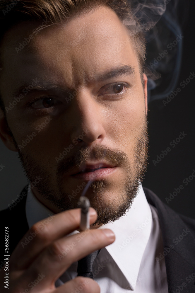 Man smoking. Bossy young man in formalwear smoking while standin Man smoking. Bossy young man in formalwear smoking while standin