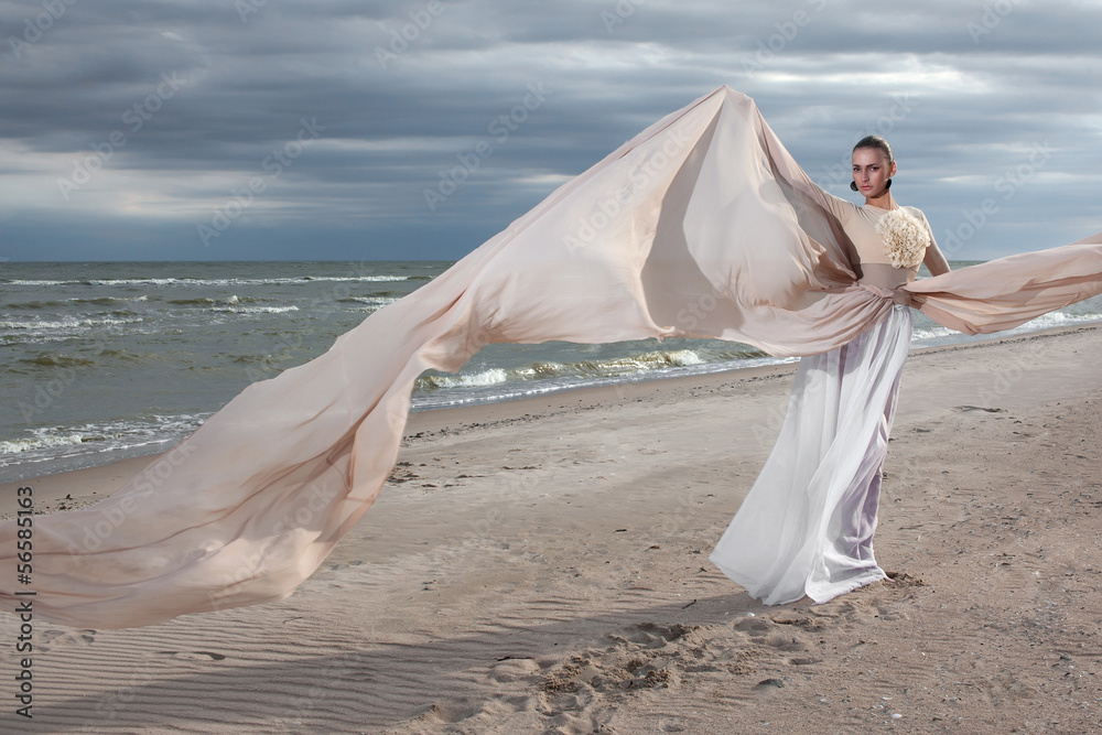 model in long beige dress posing dynamic in  waving fabric