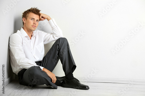 Young businessman sitting on floor, on gray wall background