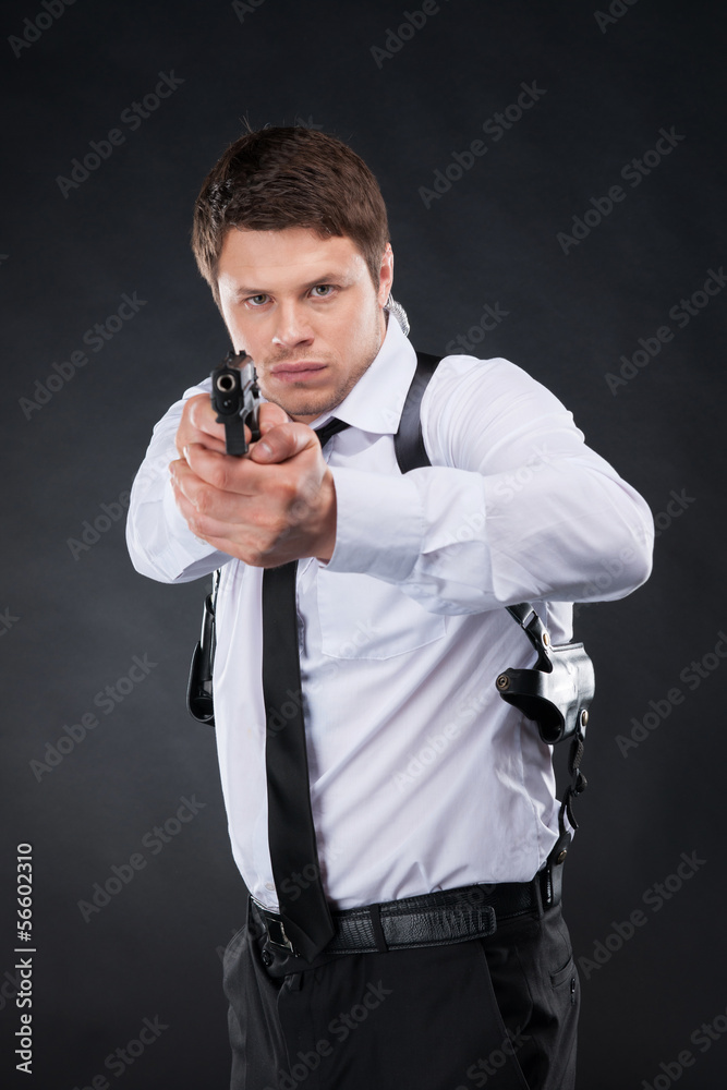 Naklejka premium Bodyguard. Confident young man in shirt and tie holding gun and