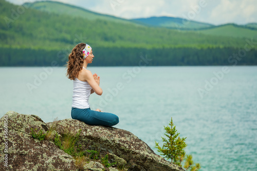 Young woman is practicing yoga at mountain lake © Maygutyak