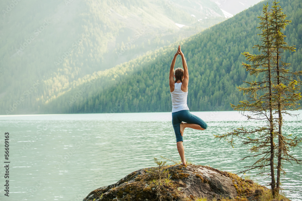 Young woman is practicing yoga at mountain lake - obrazy, fototapety, plakaty 
