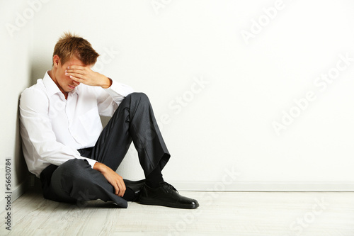 Young businessman sitting on floor, on gray wall background