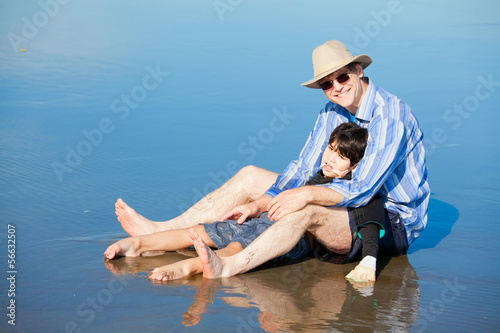 Father playing with disabled son on beach, holding him upright