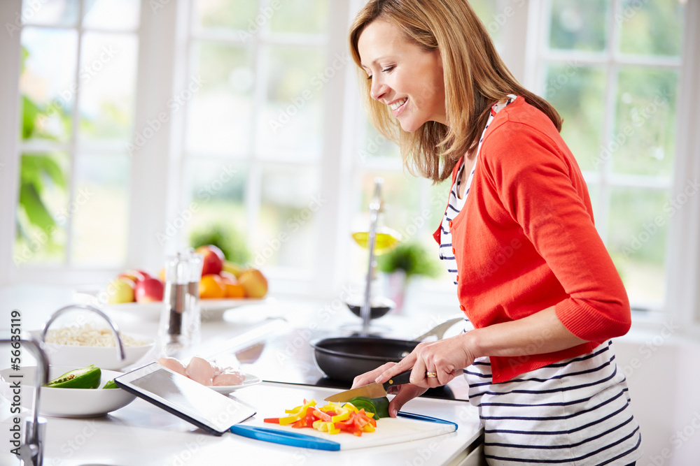 Woman In Kitchen Following Recipe On Digital Tablet