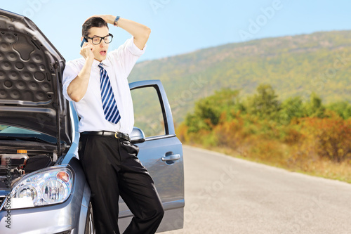 Young sad male on a broken car talking on a phone
