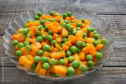 Boiled carrots with green peas in glass bowl