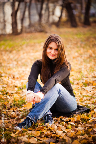 young woman sits on leaves in autumn park