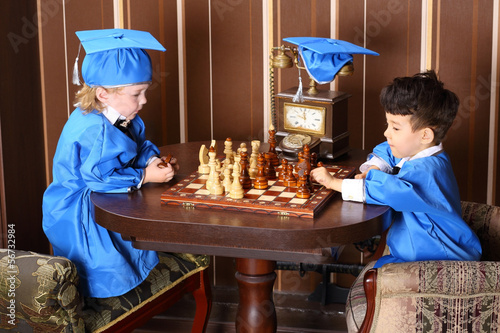 Two thoughtful boys in blue suits play chess