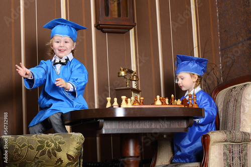 Happy little girl and boy in blue suits play chess photo