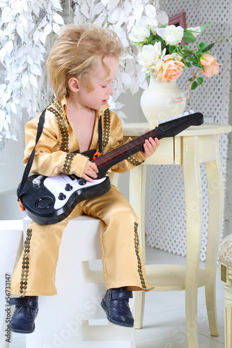 Portrait of a little boy in pop retro suit playing the guitar