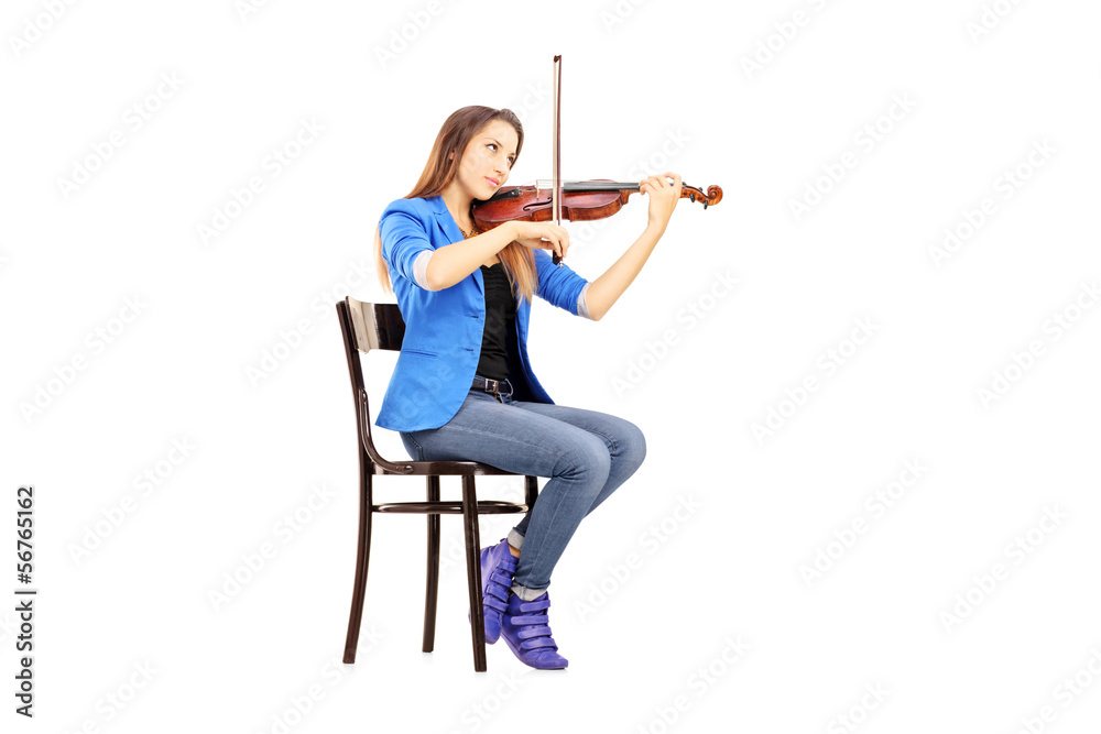 Casual young woman seated on a wooden chair playing the violin Casual young woman seated on a wooden chair playing the violin