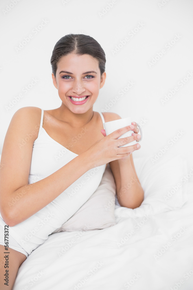 Smiling young brown haired model in white pajamas drinking coffe Smiling young brown haired model in white pajamas drinking coffe