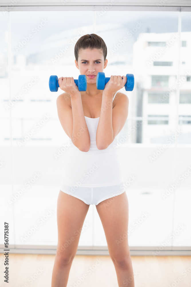 Frowning natural brown haired woman in white sportswear exercisi