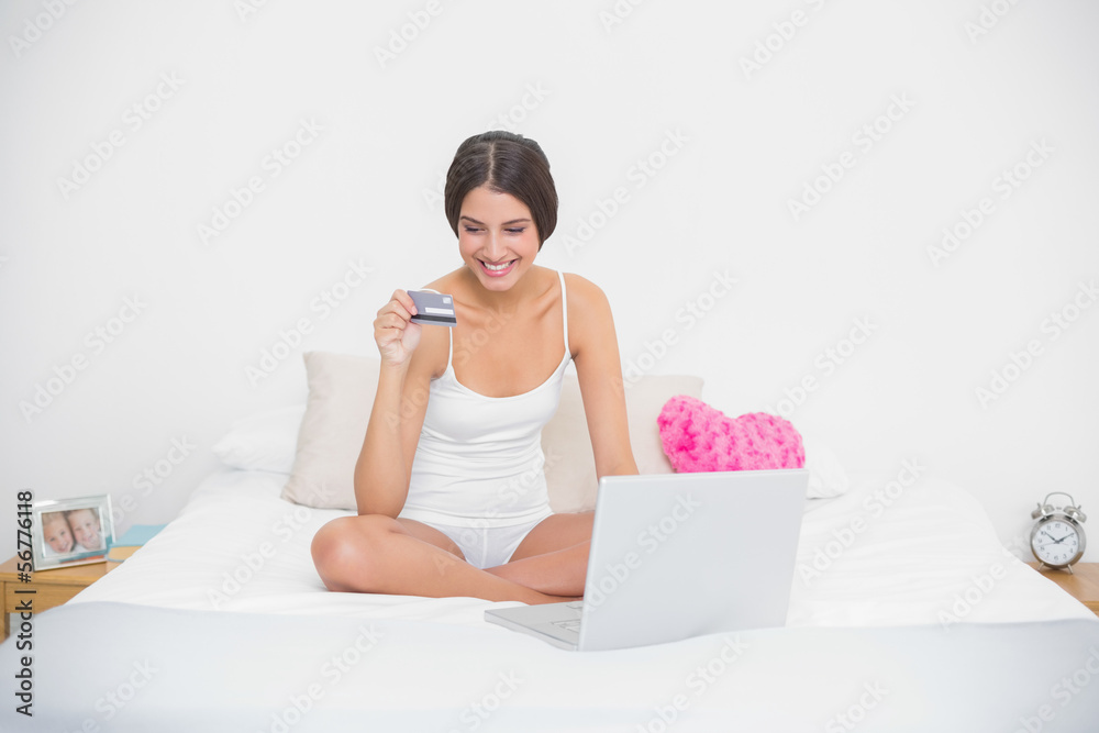 Smiling young brown haired model in white pajamas shopping onlin Smiling young brown haired model in white pajamas shopping onlin