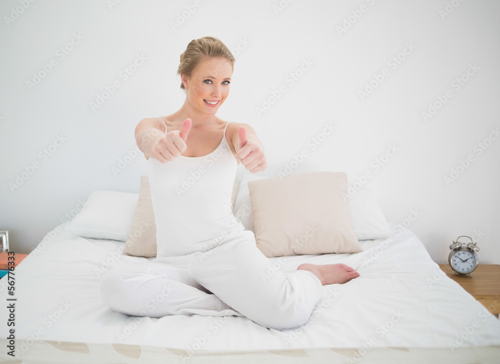 Natural smiling blonde showing thumbs up while sitting on bed Natural smiling blonde showing thumbs up while sitting on bed