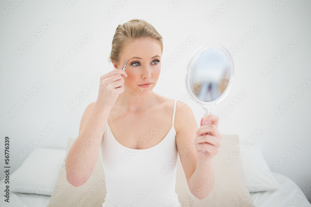 Natural serious blonde holding mirror and using tweezers Natural serious blonde holding mirror and using tweezers