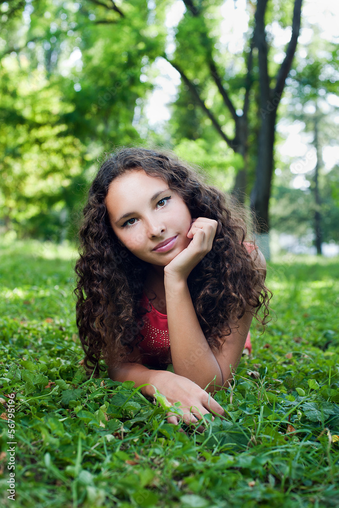 Smiling teenage girl with curly hair lying on a green grass Smiling teenage girl with curly hair lying on a green grass