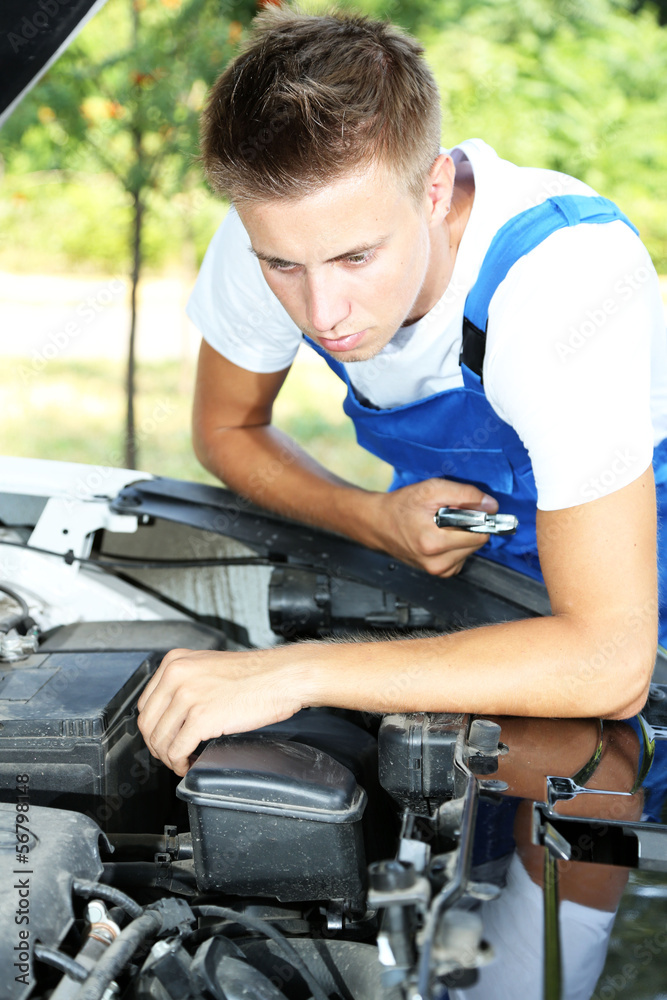 Young auto mechanic repairing car engine outdoors