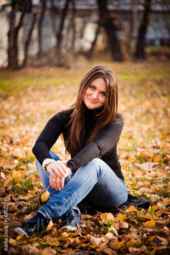 young woman sits on leaves in autumn park