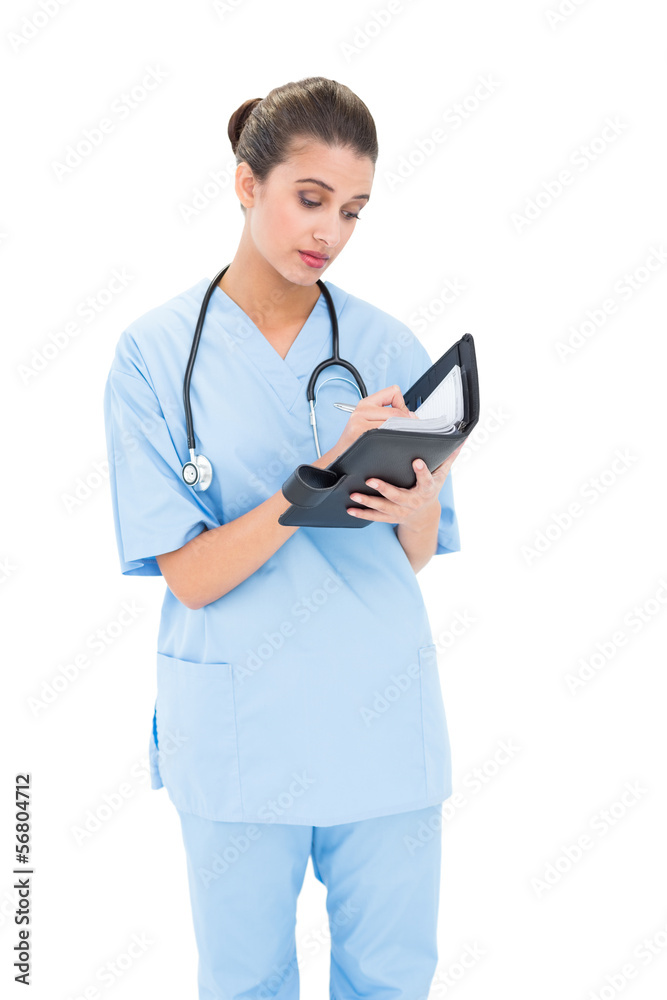 Concentrated brown haired nurse in blue scrubs filling an agenda Concentrated brown haired nurse in blue scrubs filling an agenda