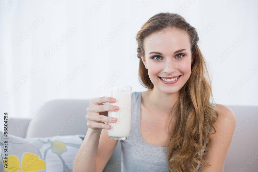 Happy young woman sitting on sofa holding glass of milk Happy young woman sitting on sofa holding glass of milk