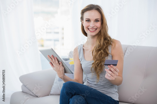 Happy young woman sitting on couch using tablet for shopping onl