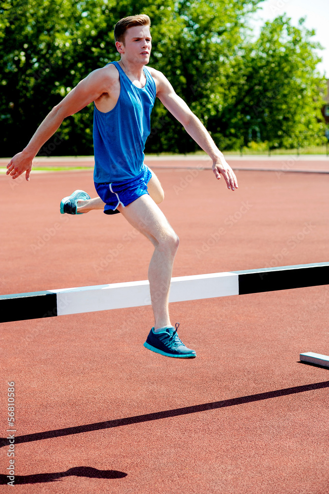 Male athlete jumping hurdle