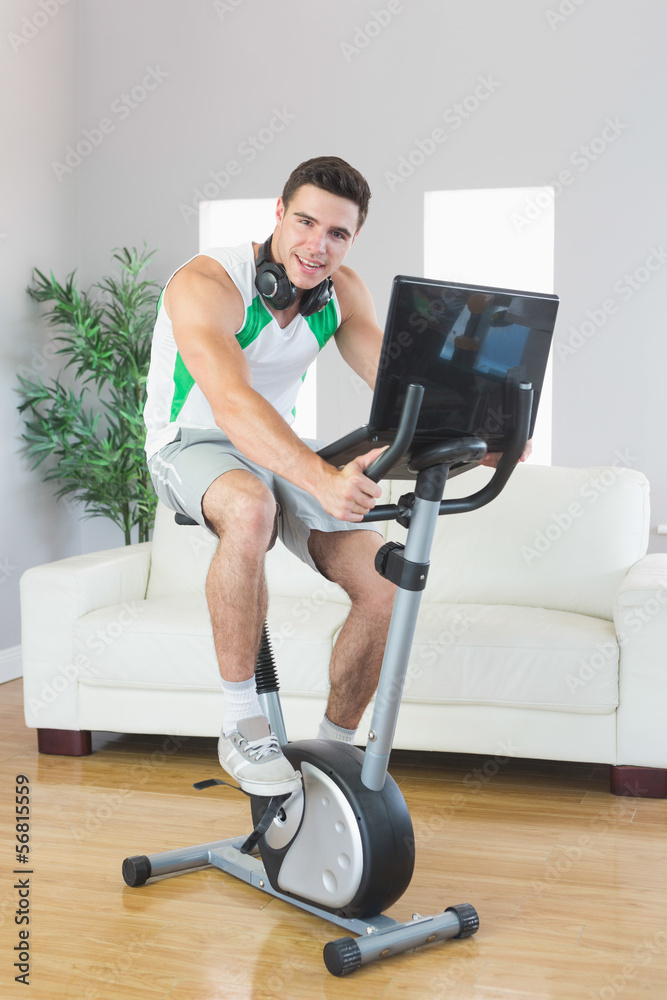 Smiling handsome man training on exercise bike using laptop Smiling handsome man training on exercise bike using laptop